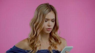 Kızgın ve hoşnutsuz sarışın kadın mor üzerine izole edilmiş akıllı telefon kullanıyor.