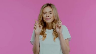 Çapraz parmaklı sarışın kadın mor üzerine izole edilmiş kameraya bakıyor.