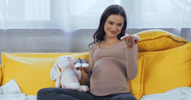 Gravid Kvinna Som Håller Babysockor Nära Mjuk Leksak Soffan — Stockvideo