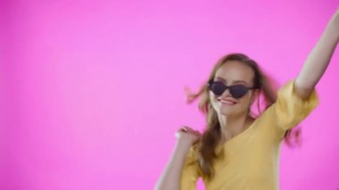 Pembe gözlüklü genç bir kadın dans ediyor.