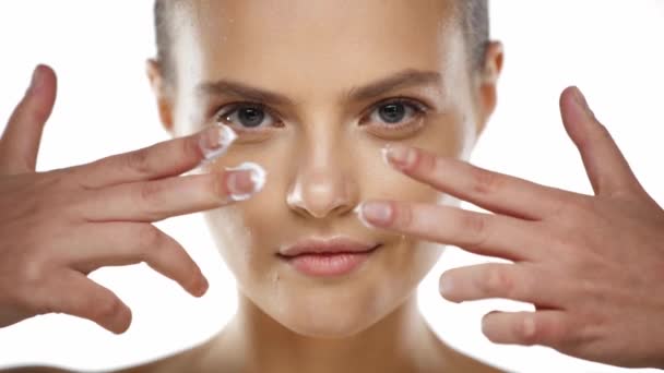 Mujer Joven Mirando Cámara Aplicación Crema Facial Las Mejillas Aisladas — Vídeos de Stock