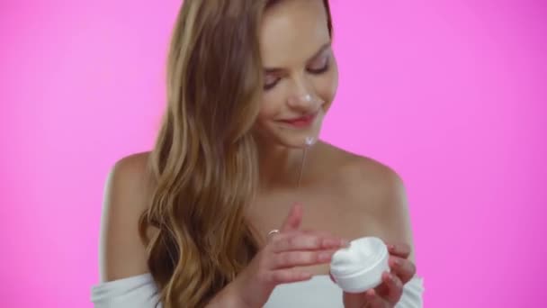 Mujer Joven Aplicando Crema Facial Mientras Posa Aislado Rosa — Vídeo de stock
