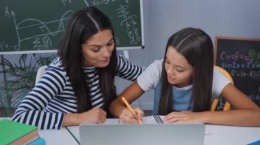Bilgisayarın yanında ödev yapan ve annesiyle konuşan bir kız.