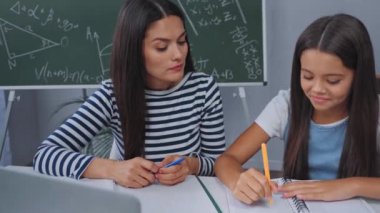 Anne ve kızı internette ders çalışırken el sallıyorlar. 