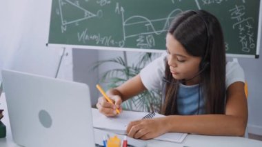 Evde internetten okurken kulaklık takan kız öğrenci.