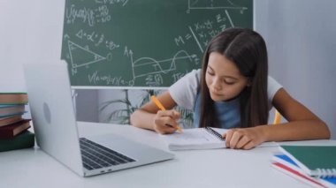 Okul çocuğu evde e-öğrenim görürken not defterinde yazıyor.