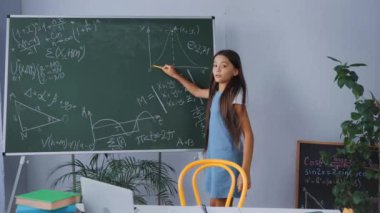 Matematik formüllerini tahtada gösterirken elinde kalem tutan çocuk 