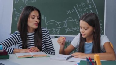 Anne okul kızıyla ödev yaparken kitap okuyor.