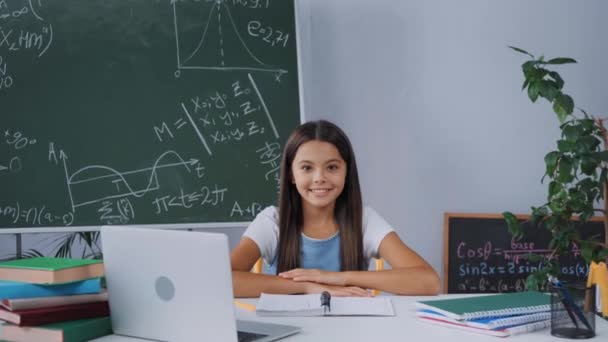 快乐的学童坐在办公桌前 手里拿着笔记本电脑 笔记本和书本 — 图库视频影像