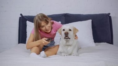 Neşeli kadın uzaktan kumandayı tutuyor ve köpeğin yanında kanalları tıklatıyor