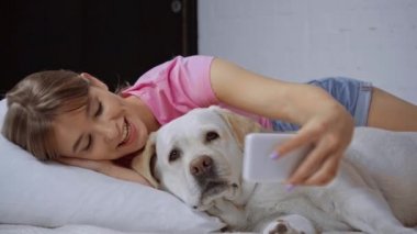 Mutlu bir kadın yastığa uzanıp Golden Retriever ile selfie çekiyor.