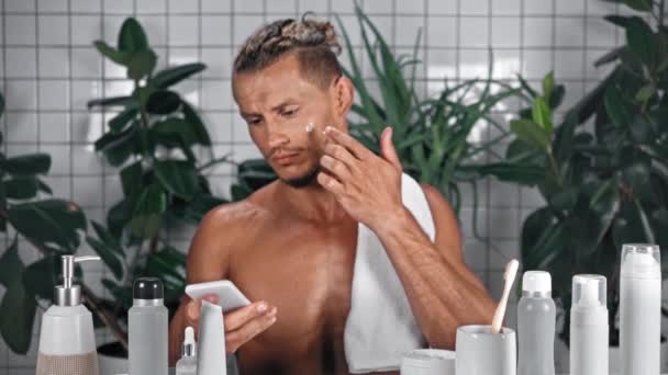 Uomo Applicando Crema Cosmetica Sul Viso Parlando Sul Telefono Cellulare — Video Stock