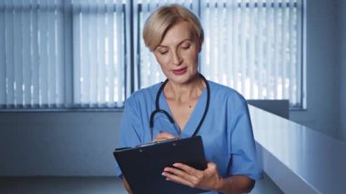 Klinikte orta yaşlı bir doktor pano tutuyor ve danışmanlık yapıyor. 