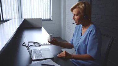 İnternette danışmanlık yaparken dizüstü bilgisayarın yanında kulaklık takan olgun bir doktor.