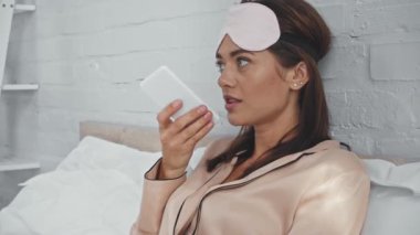 Esmer kadın yatakta oturuyor ve akıllı telefonla konuşuyor.