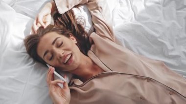 Yatakta yatarken cep telefonuyla konuşan mutlu bir kadının üst görüntüsü.