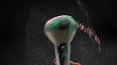 Siyah üzerine izole edilmiş kozmetik fırçasından dökülen renkli tozu kapat