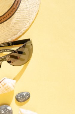 Tatil ve yaz tatili konsepti. Saman şapka, güneş gözlüğü, deniz kabukları ve sarı arka plan üzerinde çakıl düz yatıyordu. Yaz havası. Seyahat ve seyahat planlama konsepti