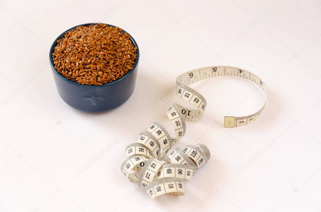 Brown flax seeds in blue ceramic bowl and centimeter on white background