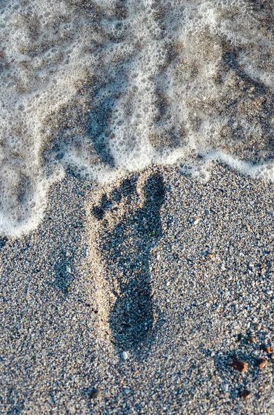 Footprint on the sand before it is washed away by the oncoming wave. Human footprint on the wet sea sand