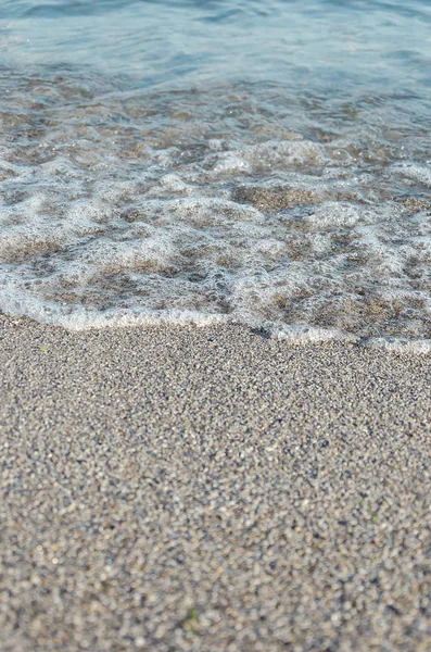 Primo piano della spiaggia sabbiosa con morbide onde in arrivo. Focus selettivo — Foto Stock