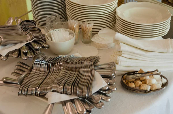 Piles of white clean plates, table knives, forks, spoons, napkins. Preparing for guest service in the restaurant