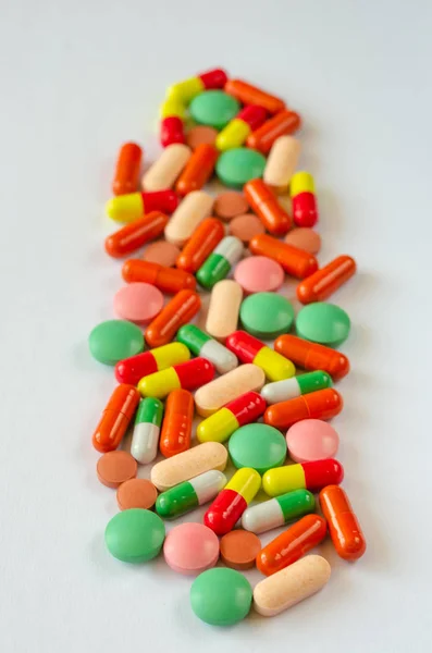 Heap de comprimidos multicoloridos, comprimidos e cápsulas em um fundo branco. Fechar os medicamentos. Vista superior — Fotografia de Stock