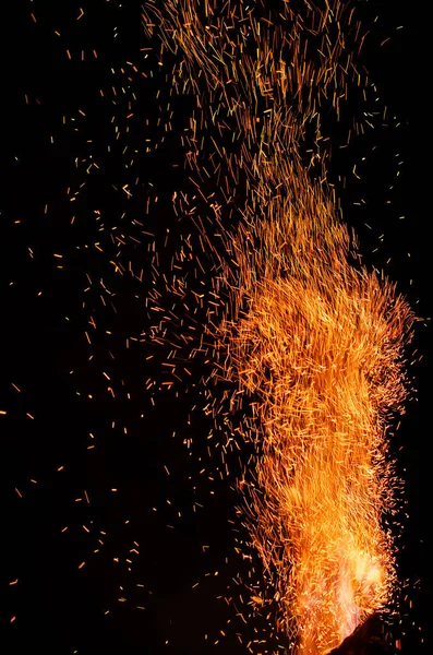 Fiamma di fuoco con scintille rosse ardenti volanti su uno sfondo nero. Particelle arancio ardente che volano via nel cielo notturno. Primo piano di bella fiamma — Foto Stock