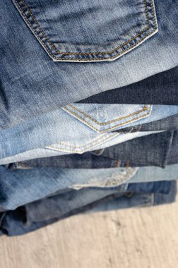 Ahşap arka plan üzerinde dikkatsizce katlanmış kot yığını. Farklı renklerde kot yakın çekim. Jeans doku veya denim arka plan. Kopyalama alanı