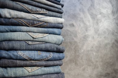 Gri arka plan üzerinde düzgünce katlanmış kadın kot yığını. Farklı renklerde kot yakın çekim. Jeans doku veya denim arka plan. Kopyalama alanı