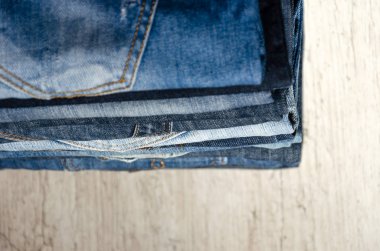 Ahşap arka plan üzerinde düzgünce katlanmış kot yığını. Farklı renklerde kot yakın çekim. Jeans doku veya denim arka plan. Kopyalama alanı