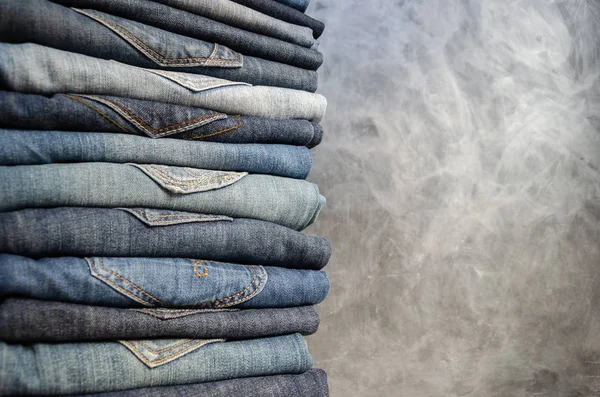 A stack of neatly folded woman's jeans on gray background. Close-up of jeans in different colors. Jeans texture or denim background. Copy space — Stock Photo, Image