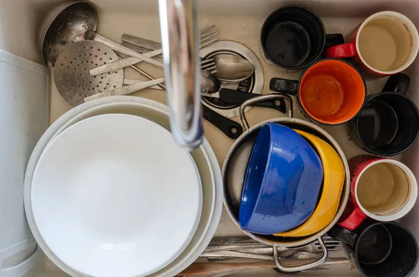 Dirty dishes in a ceramic kitchen sink. Unwashed plates, mugs and cutlery. Top view