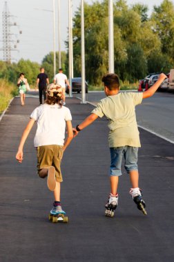 Kiev, Ukrayna - 01 Eylül 2019. Krushelnitskaya St. Holidays, tatil ve dostluk konsepti. Paten ve kaykay açık havada sürme iki aktif gençler. Gençler için boş zaman. Geri görünüm