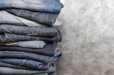 Gri arka plan üzerinde dikkatsizce katlanmış kot yığını. Farklı renklerde kot yakın çekim. Jeans doku veya denim arka plan. Kopyalama alanı