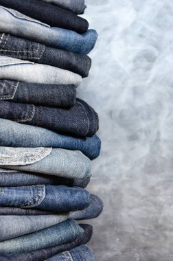 Gri arka plan üzerinde dikkatsizce katlanmış kot yığını. Farklı renklerde kot yakın çekim. Jeans doku veya denim arka plan. Kopyalama alanı