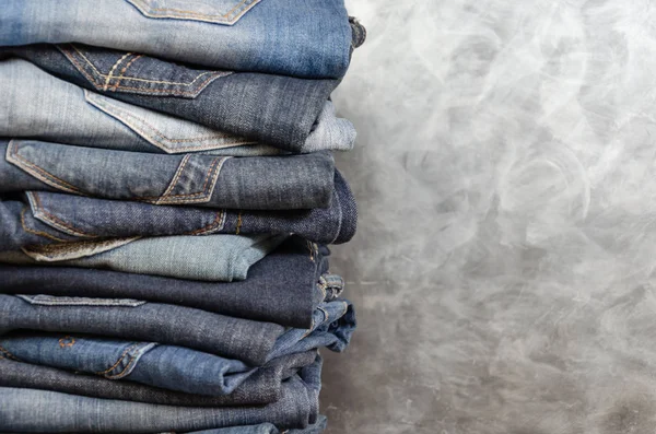 Gri arka plan üzerinde dikkatsizce katlanmış kot yığını. Farklı renklerde kot yakın çekim. Jeans doku veya denim arka plan. Kopyalama alanı