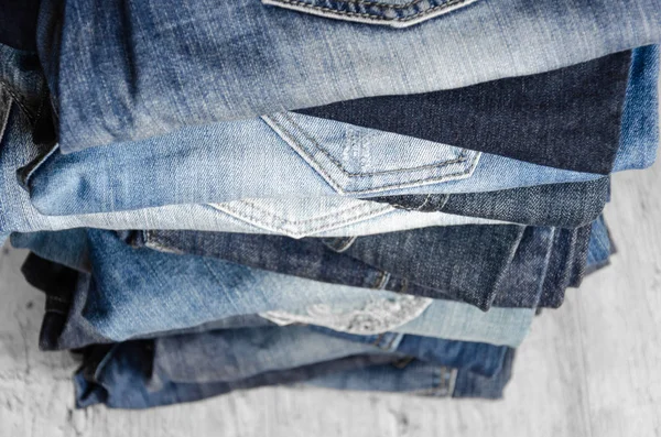 A stack of carelessly folded woman's jeans on gray background. Close-up of jeans in different colors. Jeans texture or denim background. Selective focus — Stock Photo, Image