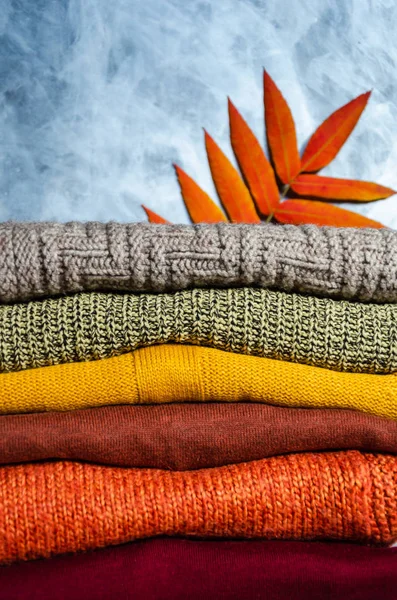 Montón de suéteres de punto tibios doblados de las mujeres en colores cálidos y hojas de otoño brillantes sobre fondo gris. Primer plano. Copiar espacio — Foto de Stock