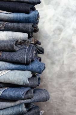 Gri arka plan üzerinde dikkatsizce katlanmış kot yığını. Farklı renklerde kot yakın çekim. Jeans doku veya denim arka plan. Kopyalama alanı