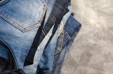 Gri arka plan üzerinde dikkatsizce katlanmış kot yığını. Farklı renklerde kot yakın çekim. Jeans doku veya denim arka plan. Kopya alanı. Seçici odaklama