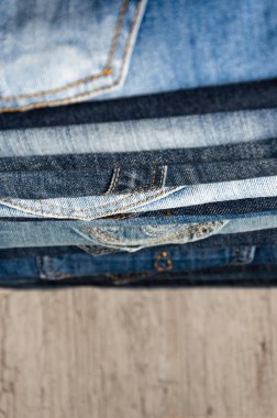 Ahşap arka plan üzerinde düzgünce katlanmış kot yığını. Farklı renklerde kot yakın çekim. Jeans doku veya denim arka plan. Kopya alanı. Seçici odaklama