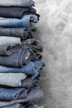 Gri arka plan üzerinde dikkatsizce katlanmış kot yığını. Farklı renklerde kot yakın çekim. Jeans doku veya denim arka plan. Kopyalama alanı