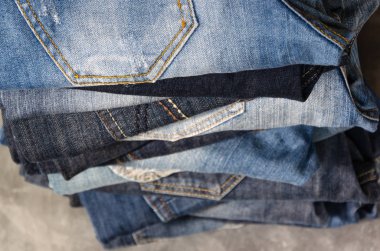 Gri arka plan üzerinde dikkatsizce katlanmış kot yığını. Farklı renklerde kot yakın çekim. Jeans doku veya denim arka plan. Seçici odaklama