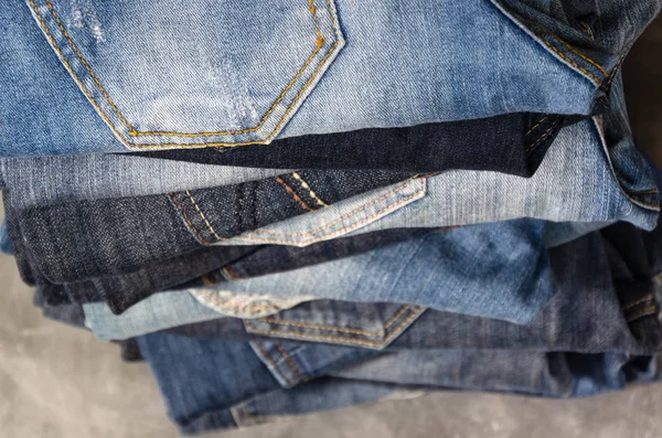 A stack of carelessly folded jeans on gray background. Close-up of jeans in different colors. Jeans texture or denim background. Selective focus — Stock Photo, Image