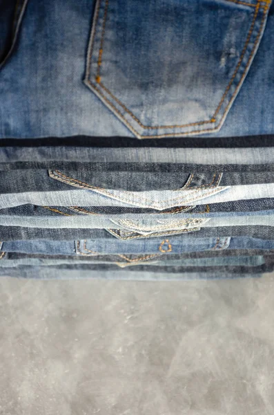 A stack of neatly folded jeans on gray background. Close-up of jeans in different colors. Jeans texture or denim background. Copy space. Selective focus — Stock Photo, Image