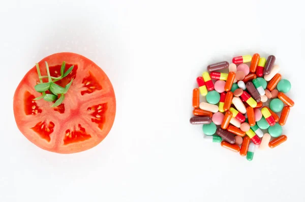 Свежие овощи против таблеток. Кусок помидоров и свежие ростки подсолнечника на куче разноцветных таблеток на белом фоне. Концепция здорового питания. Копирование пространства — стоковое фото