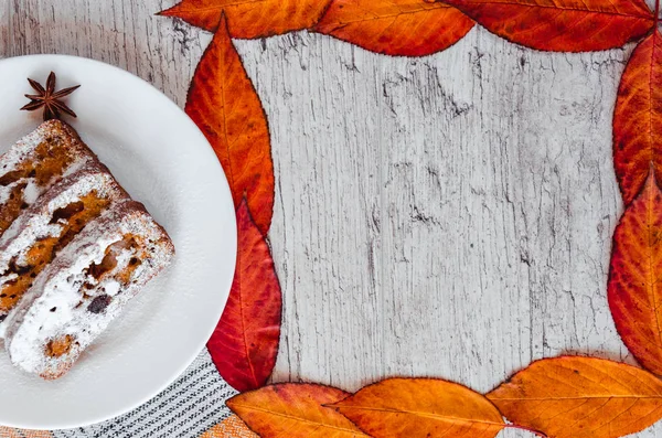 Homemade carrot cake with walnuts and dried fruits, sprinkled with powdered sugar. Frame of autumn leaves. Healthy desserts. Healthy eating concept. Copy space — Stock Photo, Image