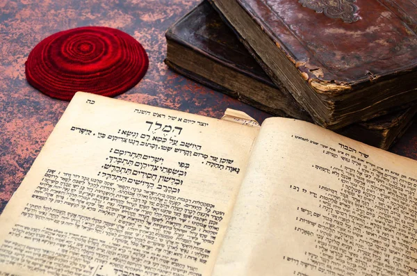 Jewish Bible. A stack of old leather-bound Jewish books with gold stamping and red knitted jewish bale. One book is open. Closeup of Hebrew text. Selective focus — Stock Photo, Image