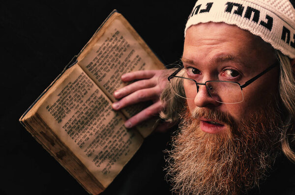 A Hasidic Jew reads Siddur. Religious orthodox Jew with a red beard and with pace in a white bale praying. On the bale is an inscription Rabbi Nahman from Uman. Closeup